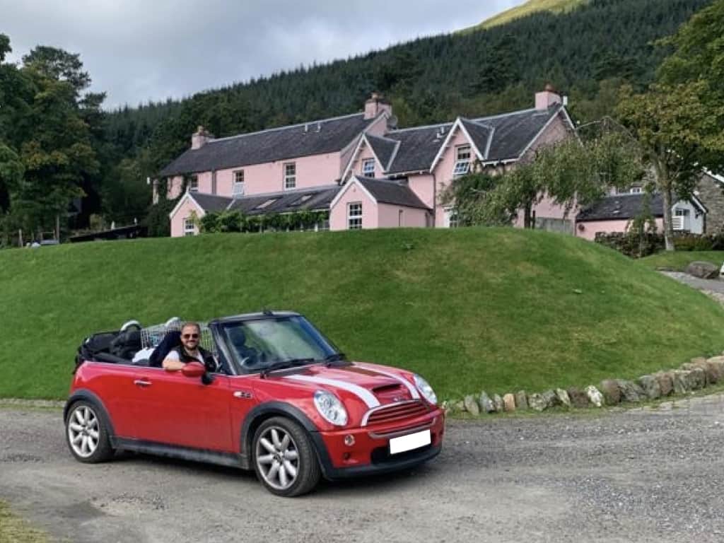 red mini convertible with a luggage rack fitted hood down outside a pink house
