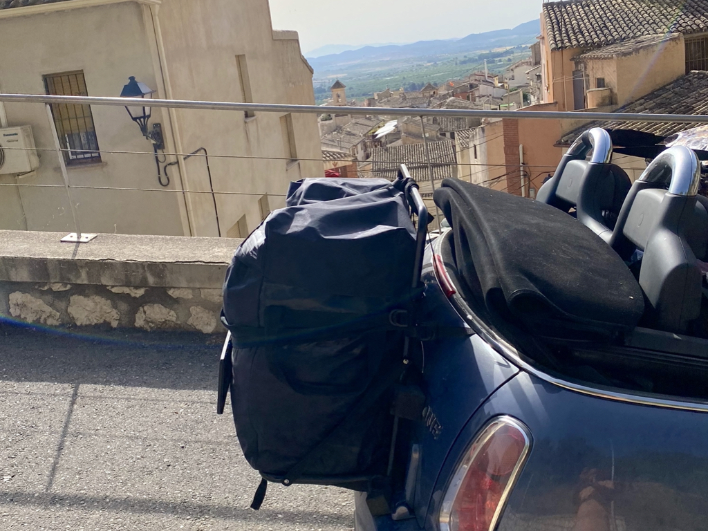 mini convertibel with the roof down and a hatch-bag luggage rack fitted in a spanish village overlooking old houses