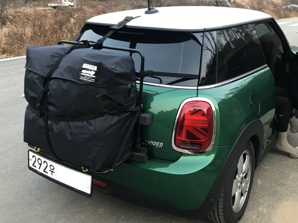 Green mini copper on a country road with a hatch-bag roof box rack fitted to the rear